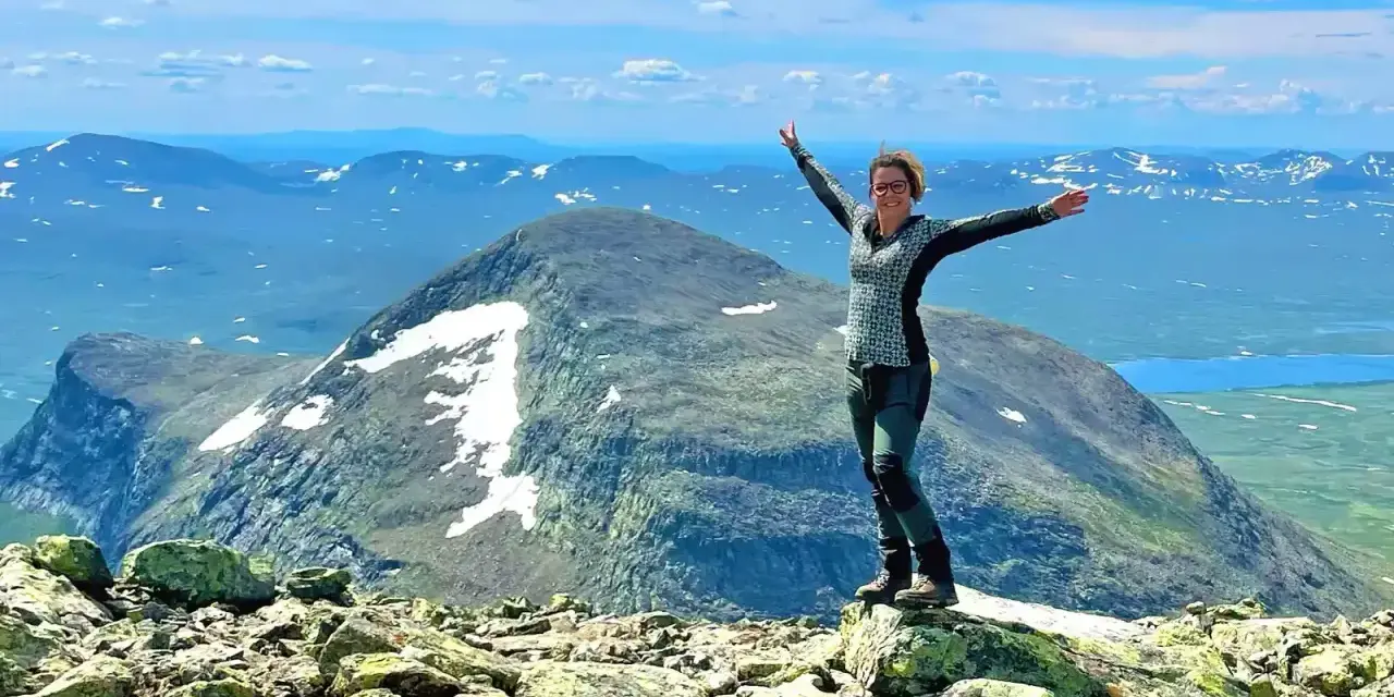 Lycklig vandrare på en bergstopp med vidsträckt utsikt över fjällandskap. Här finns fina vandringsleder för alla.