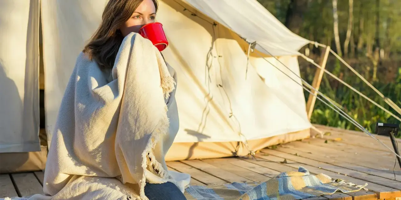 Kvinna med filt och röd mugg vid tältet. En perfekt packlista camping-morgon.
