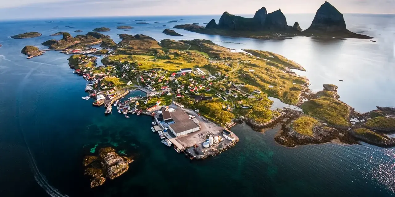 En pittoresk by på en ö i Norge, med berg i bakgrunden. En båt lämnar ett spår i vattnet. En vacker vy över traena norge.