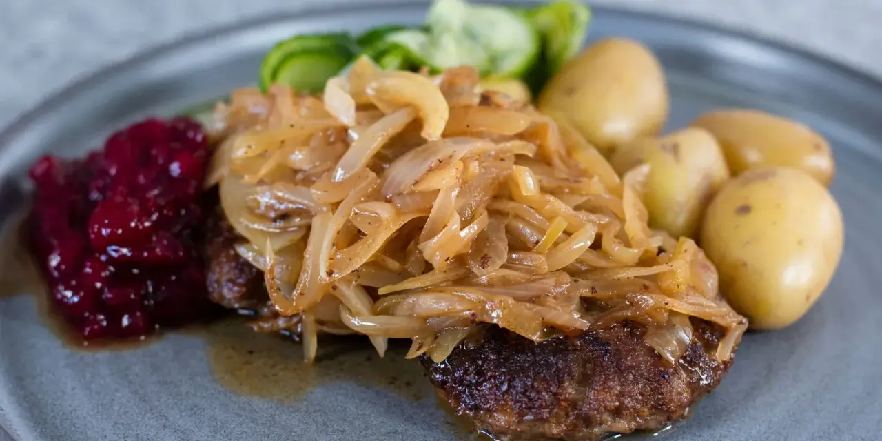 En tallrik med pannbiff, stekt lök, lingonsylt och kokt potatis. Ett klassiskt svenskt pannbiff recept som är lätt att lyckas med.