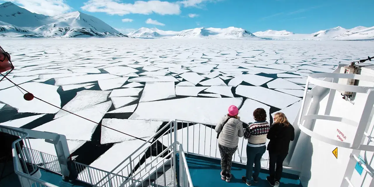 Besök Svalbard och se isflak som bryts upp i ett arktiskt landskap. Tre personer står på ett fartyg och blickar ut över det frusna havet.