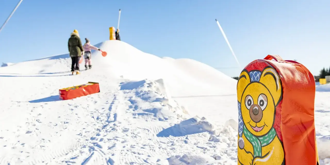 En glad björn pryder en pulka backe. Barn klädda för kyla väntar på sin tur att åka nerför den snöiga kullen.