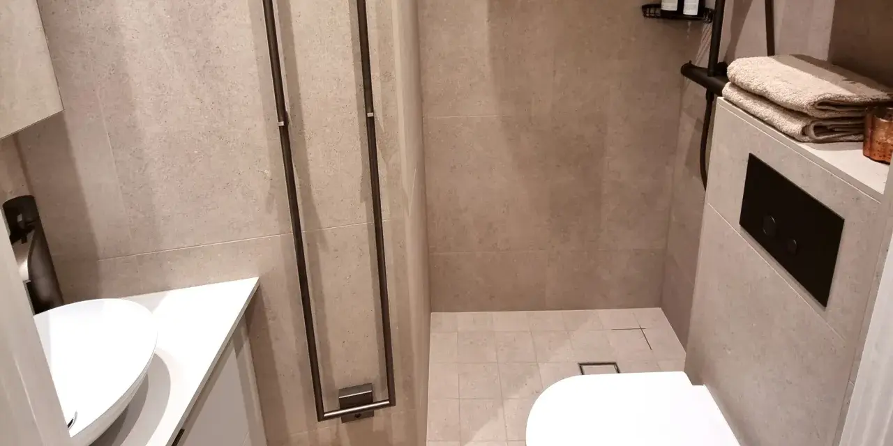 Modernt och stilrent små badrum inspiration med dusch, handfat och vägghängd toalett. Ljusbeige kakel ger en lugn känsla.