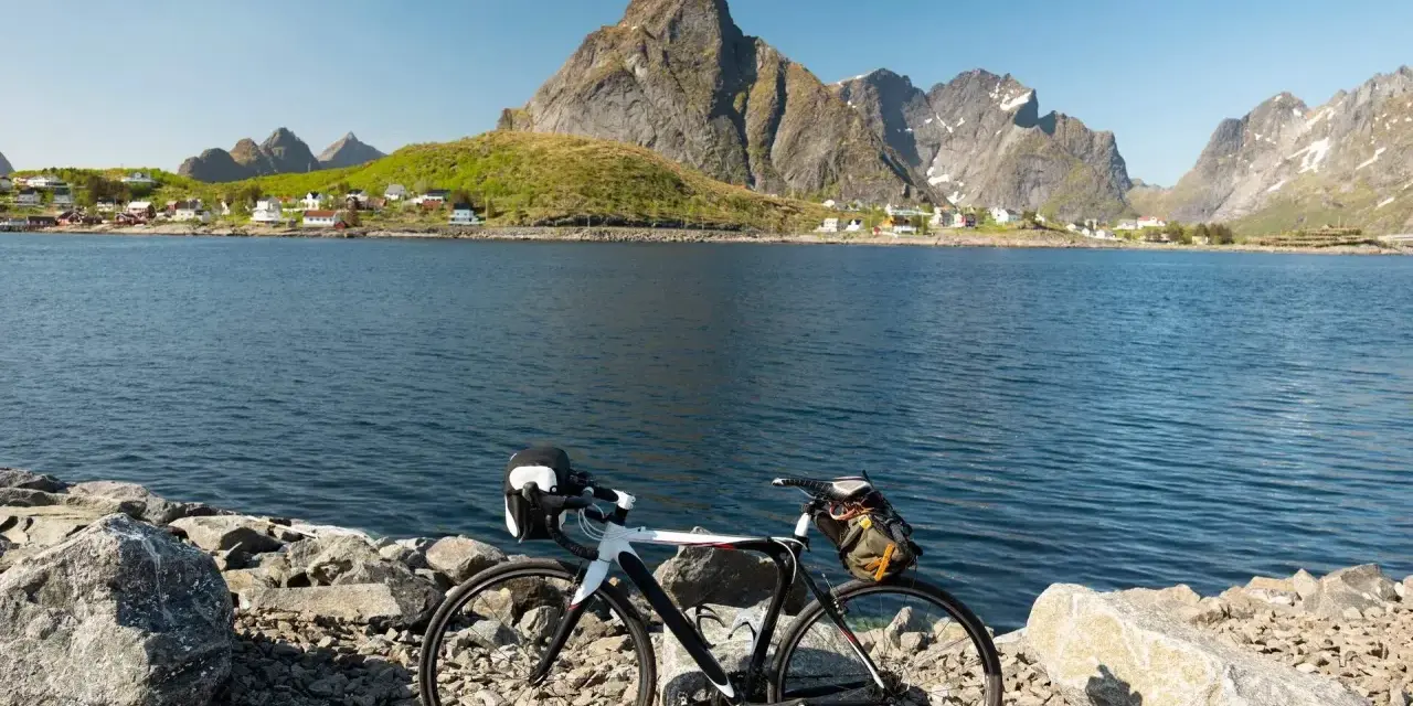 En cykel står vid en sjö med berg och en by i bakgrunden. Perfekt för mtb norge-äventyr.