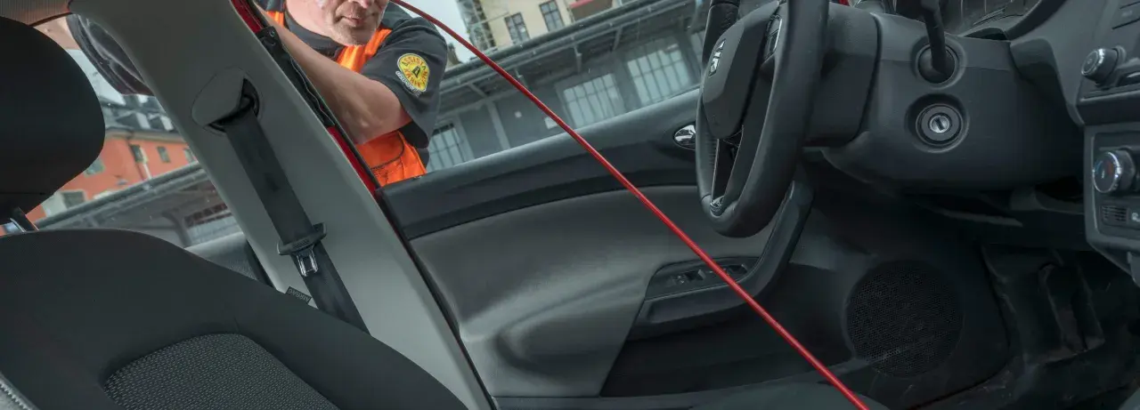 En person i orange väst använder ett rött verktyg för att öppna en bildörr. Kanske glömde de dnt nyckel därinne.