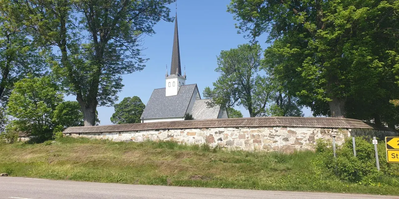 Kyrka med spira bakom stenmur och träd. En skylt visar "2 St". Kanske en vy från Hamar, Norge.