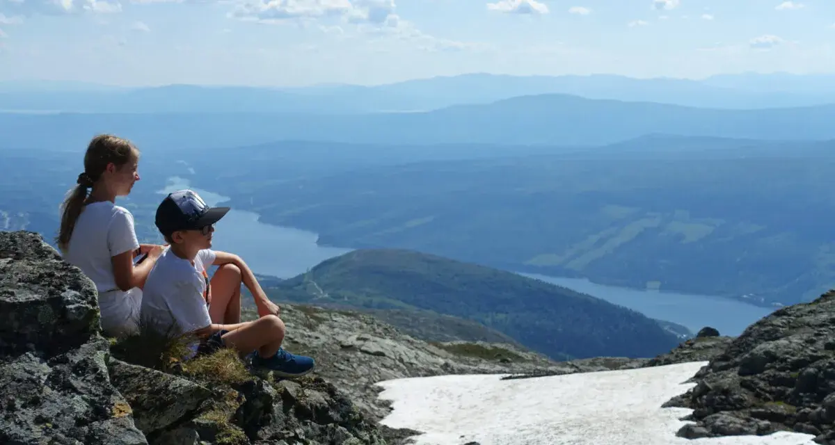 Två barn vilar på en klippa med utsikt över en sjö och berg. Perfekt för vandringsleder i Åre.