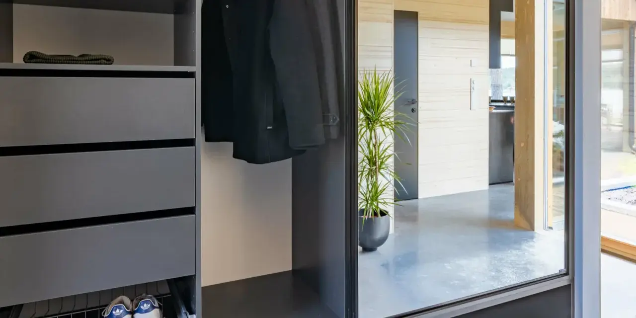 Snygga inredningstips hall: mörk garderob med rockar, mössor, skor och en grön växt som speglas i en stor glasdörr.