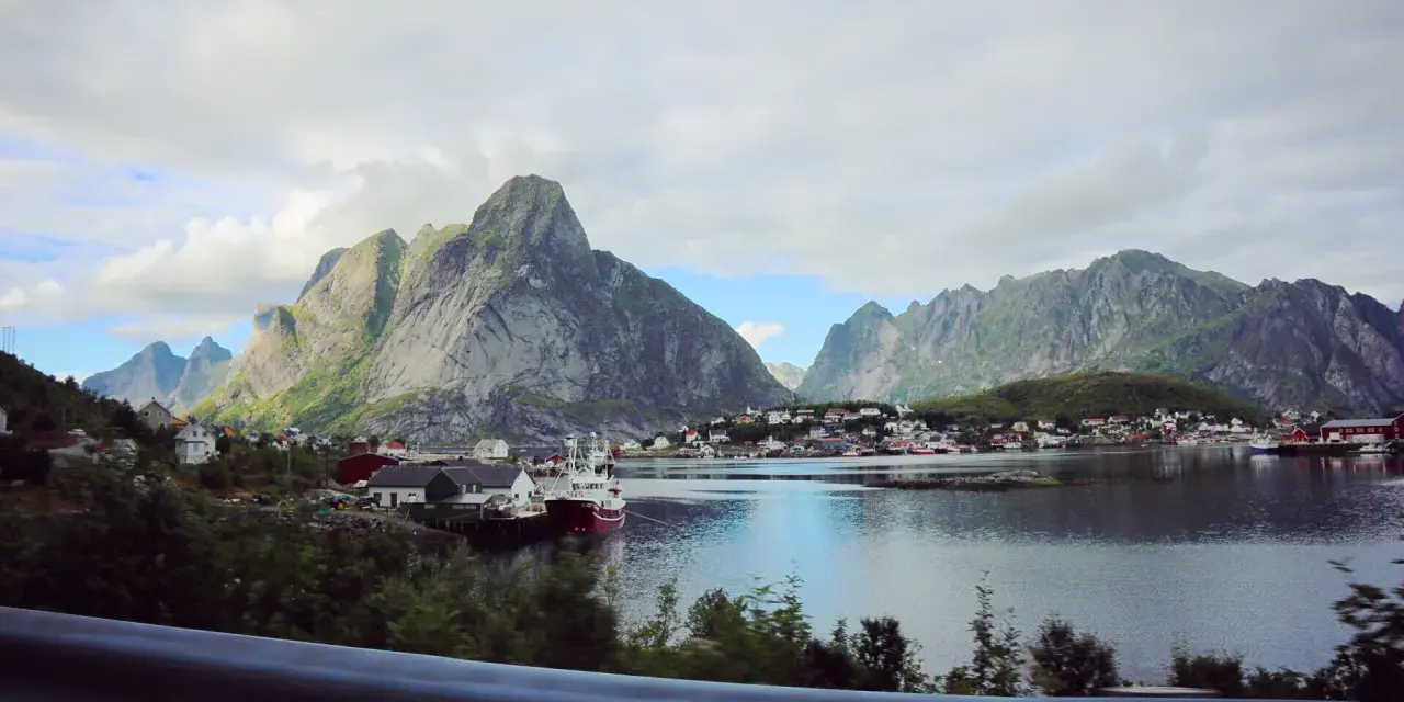 Vacker vy över en by vid vattnet, omgiven av dramatiska berg. Kanske en vy från Narvik mot Lofoten?