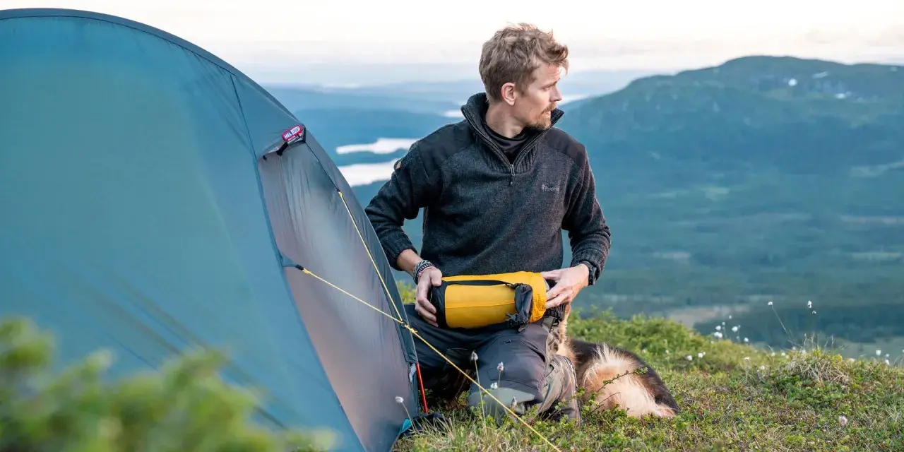 Man med hund packar för vandring. En gul sovsäck ligger redo. Perfekt packlista vandring dagstur.