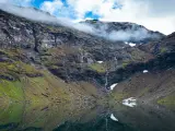 En spegelblank sjö reflekterar en dramatisk bergssida med en forsande vattenfall. Perfekt för att vandra i Abisko.