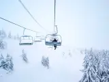 En skidåkare åker linbana uppför ett snötäckt berg i Norge, omgiven av frostiga träd.