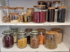 Snyggt organiserat skafferi med glasburkar fyllda med nötter, torkad frukt, frön och baljväxter. Enkelhet och ordning för att organisera skafferi.