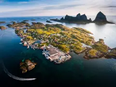 En pittoresk by på en ö i Norge, med berg i bakgrunden. En båt lämnar ett spår i vattnet. En vacker vy över traena norge.
