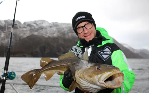 Glad fiskare visar upp en stor torsk fångad i Norge.