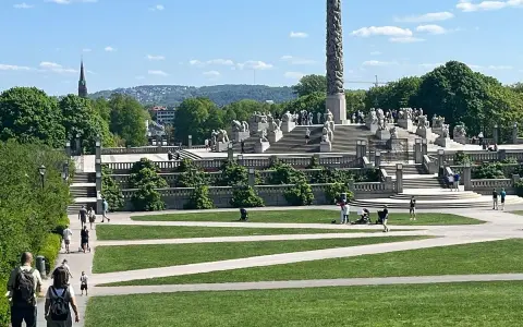 Vigelandsparken med dess imponerande monoliten och skulpturer, en solig dag med besökare som njuter av parken.