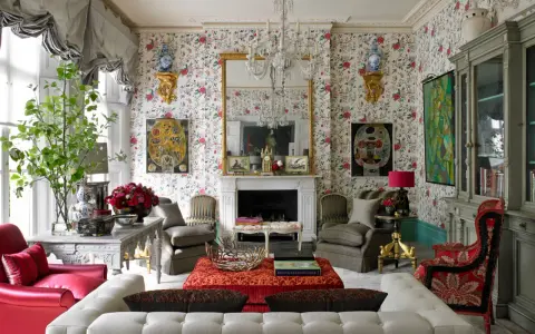 Maximalism inredning med blommig tapet, kristallkrona, röda och grå möbler samt konstverk.