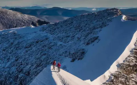 Två vandrare på en snöig bergskam, redo att bestiga Kebnekaise. Vacker utsikt över fjällen.