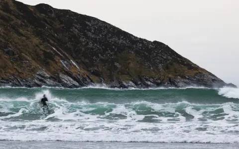 En ensam surfare kämpar mot en kraftig våg vid kusten i Norge. Den dramatiska bergssidan bakom ger en mäktig kuliss för detta äventyr.