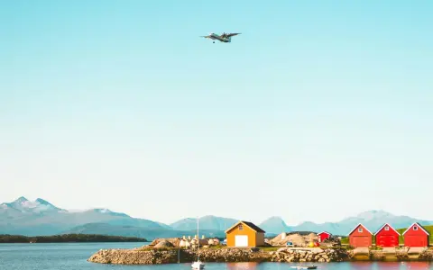Ett flygplan närmar sig landning vid Molde, Norge. Röda och gula bodar står vid vattnet med berg i bakgrunden.