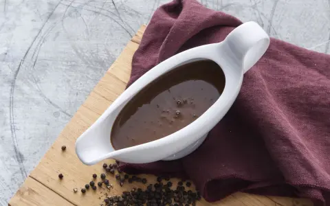 En vit såsslev fylld med mustig brunsås, bredvid en hög med svartpepparkorn. Ett perfekt brunsås recept för middagen.