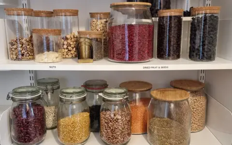 Snyggt organiserat skafferi med glasburkar fyllda med nötter, torkad frukt, frön och baljväxter. Enkelhet och ordning för att organisera skafferi.