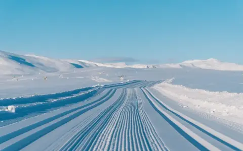 Perfekt preparerade spår för längdskidåkning i Hemsedal. Solen lyser på de snötäckta bergen och den blå himlen.