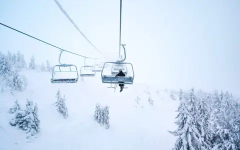 En skidåkare åker linbana uppför ett snötäckt berg i Norge, omgiven av frostiga träd.