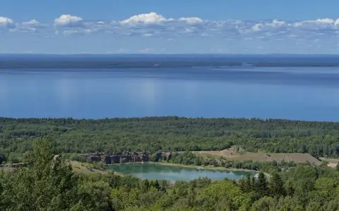 Vacker utsikt över en sjö och en grönskande skog. En liten sjö med klippor syns i mitten, en del av **Götaleden etapp 7**.