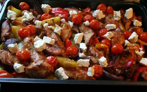 En härlig grekisk pyttipanna med kyckling, potatis, tomater, paprika och fetaost i en ugnsform.
