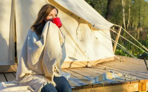 Kvinna med filt och röd mugg vid tältet. En perfekt packlista camping-morgon.