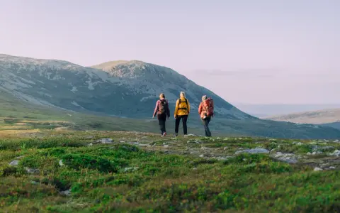 Tre personer på vandring i Idre fjällandskap. Solen lyser på de böljande kullarna och fjällen i bakgrunden.