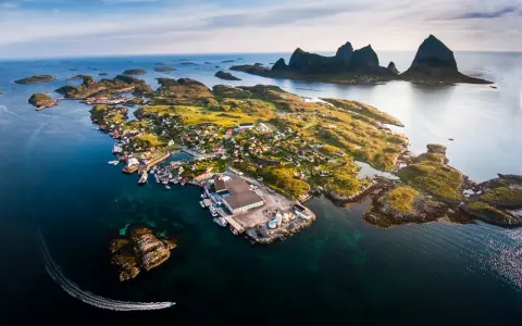 En pittoresk by på en ö i Norge, med berg i bakgrunden. En båt lämnar ett spår i vattnet. En vacker vy över traena norge.