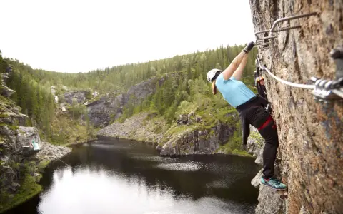 En person klättrar på en klippa vid rypetoppen adventurepark. Vacker natur med sjö och skog.