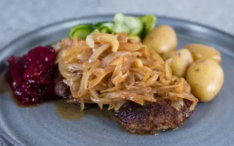 En tallrik med pannbiff, stekt lök, lingonsylt och kokt potatis. Ett klassiskt svenskt pannbiff recept som är lätt att lyckas med.