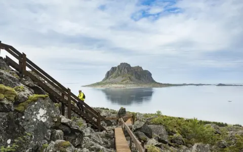 Vandrare på trappor vid havet med en imponerande bergstopp i bakgrunden, en vy från Vega Norge.