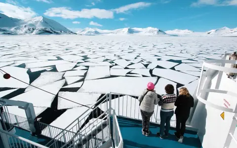 Besök Svalbard och se isflak som bryts upp i ett arktiskt landskap. Tre personer står på ett fartyg och blickar ut över det frusna havet.