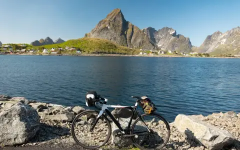 En cykel står vid en sjö med berg och en by i bakgrunden. Perfekt för mtb norge-äventyr.