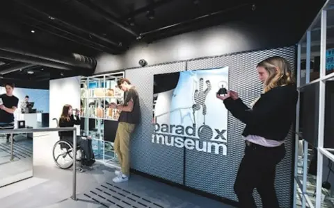 Besökare utforskar utställningar på Paradox Museum Oslo. En kvinna i rullstol tittar på sin telefon.