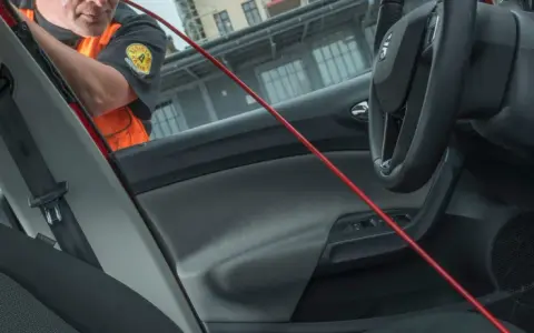 En person i orange väst använder ett rött verktyg för att öppna en bildörr. Kanske glömde de dnt nyckel därinne.