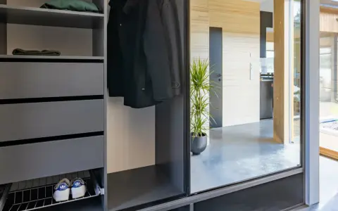 Snygga inredningstips hall: mörk garderob med rockar, mössor, skor och en grön växt som speglas i en stor glasdörr.