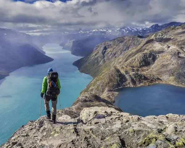 Vandrare med ryggsäck står på en klippa och blickar ut över turkosa sjöar och berg i Jotunheimen nationalpark.