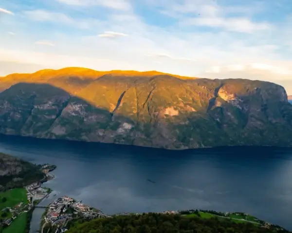 En vy över Sognefjorden med solbelysta berg och en liten by vid vattnet. Som en levande sognefjorden karta.