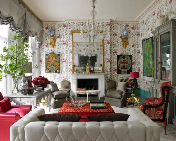 Maximalism inredning med blommig tapet, kristallkrona, röda och grå möbler samt konstverk.