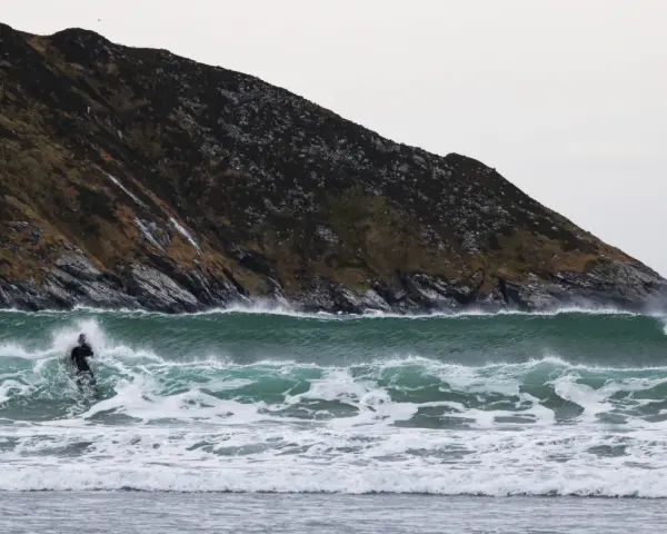 En ensam surfare kämpar mot en kraftig våg vid kusten i Norge. Den dramatiska bergssidan bakom ger en mäktig kuliss för detta äventyr.