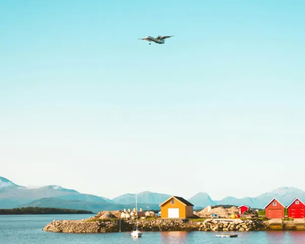 Ett flygplan närmar sig landning vid Molde, Norge. Röda och gula bodar står vid vattnet med berg i bakgrunden.