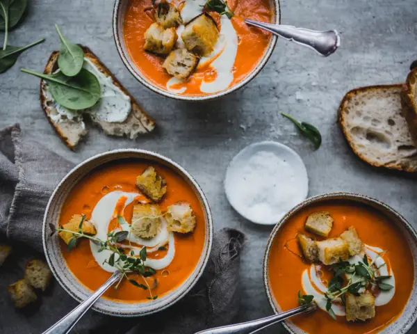 Tre skålar med krämig tomatsoppa, toppad med krutonger och en virvel av grädde. Perfekt för ett mysigt tomatsoppa recept.