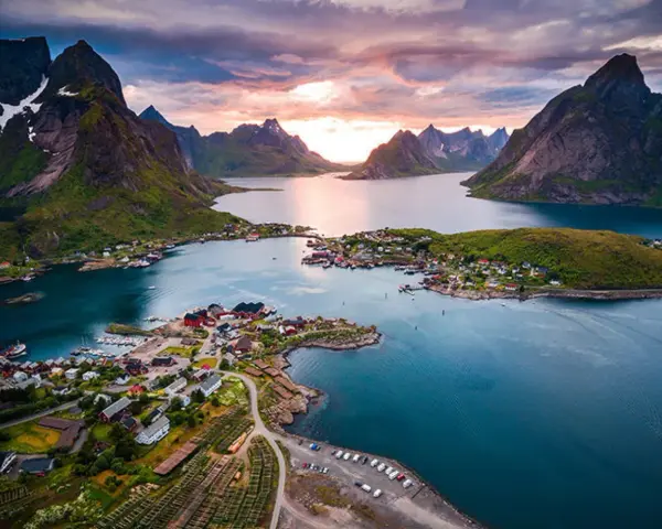 En pittoresk by med röda hus vid en fjord, omgiven av dramatiska berg. En av de fina platserna i Norge, badande i solnedgångens ljus.