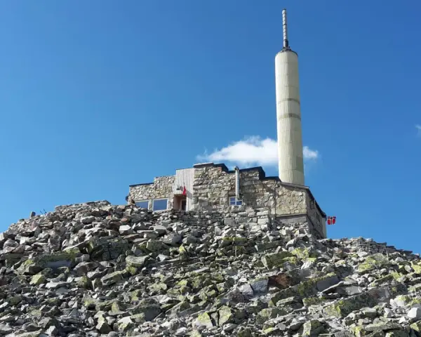 Stone building with a tall tower on a rocky mountain peak under a blue sky.