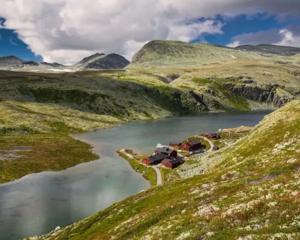 En vacker vy över en sjö med röda stugor vid en fjällsluttning, perfekt för en triangeltur i Norge.
